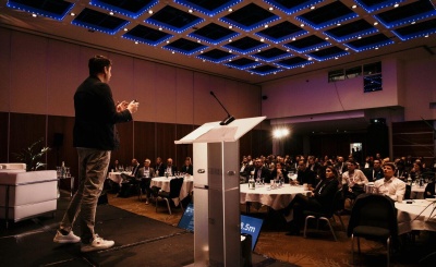 A man stands at a podium, delivering a speech to an audience at a professional conference.