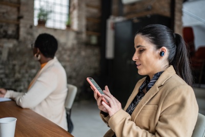 Visually impaired businesswoman using smartphone and earphones during business meeting