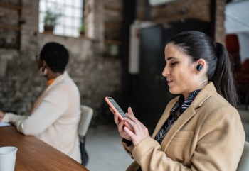 Visually impaired businesswoman using smartphone and earphones during business meeting