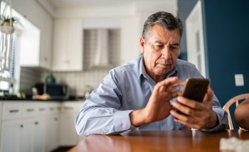 A man sits at a table, focused on his phone, with a thoughtful expression on his face.