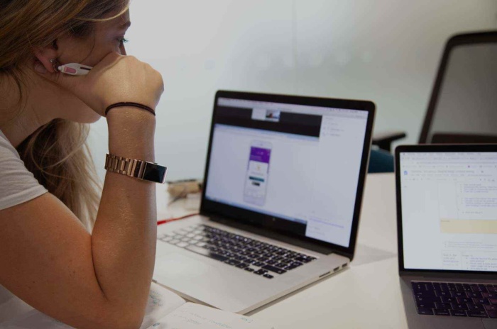 A woman rests her elbow on a white desk whilst looking at digital designs on a laptop screen