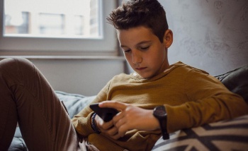 Teenager using their phone in their bedroom whilst leaning on a pillow and lying upright on a sofa